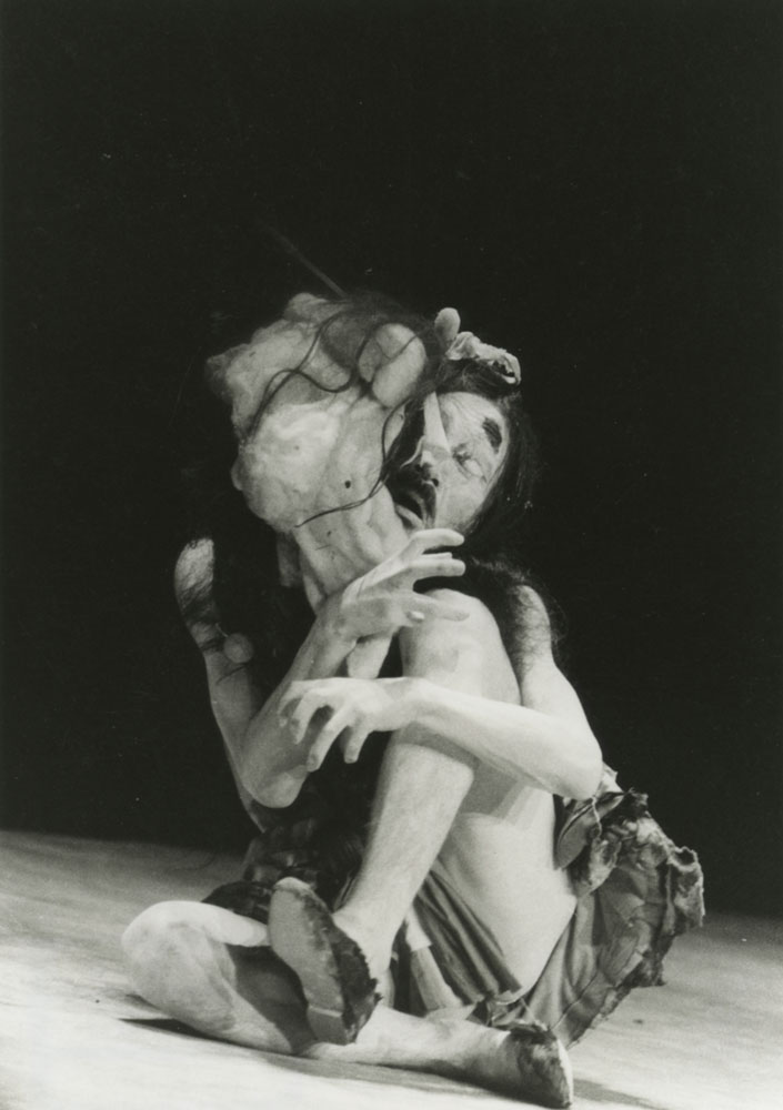 Master Butoh Dancer Tatsumi Hijikata in a contorted sitting position while a grotesque mask rests on his face
